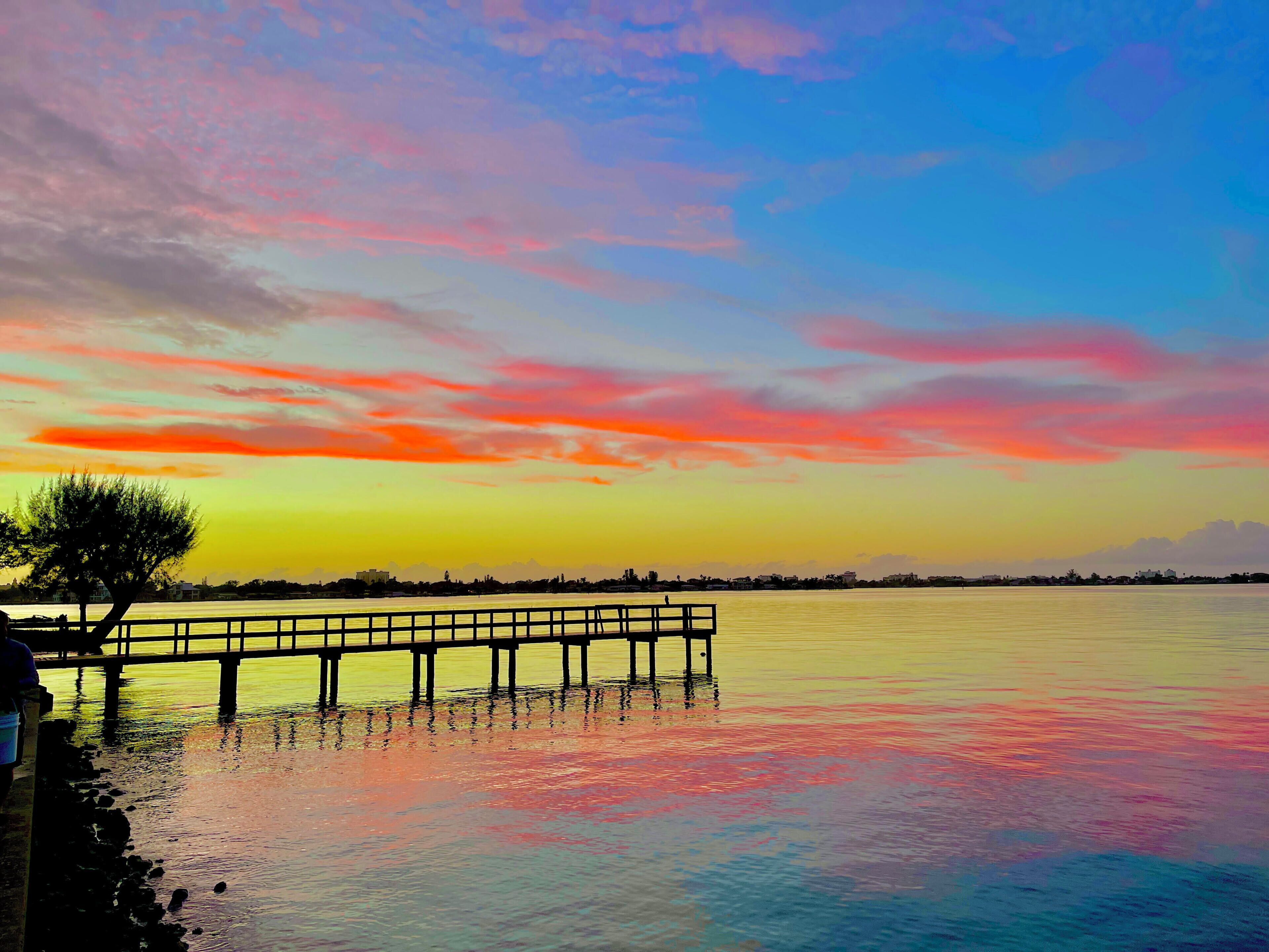 A pier extending into calm water with a sunset sky.
