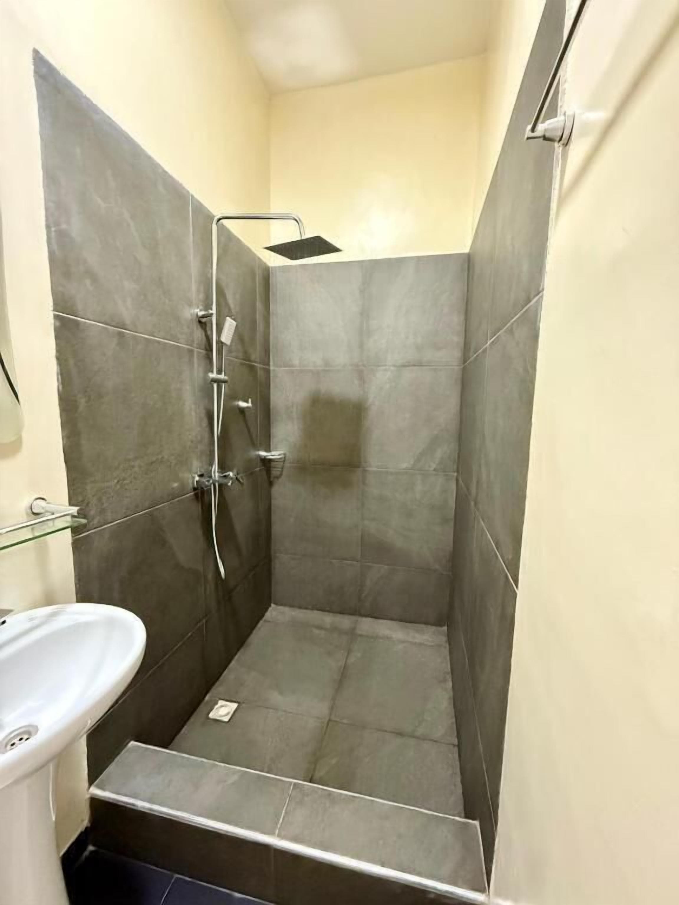 A small, enclosed shower area with a white sink and tiled walls.