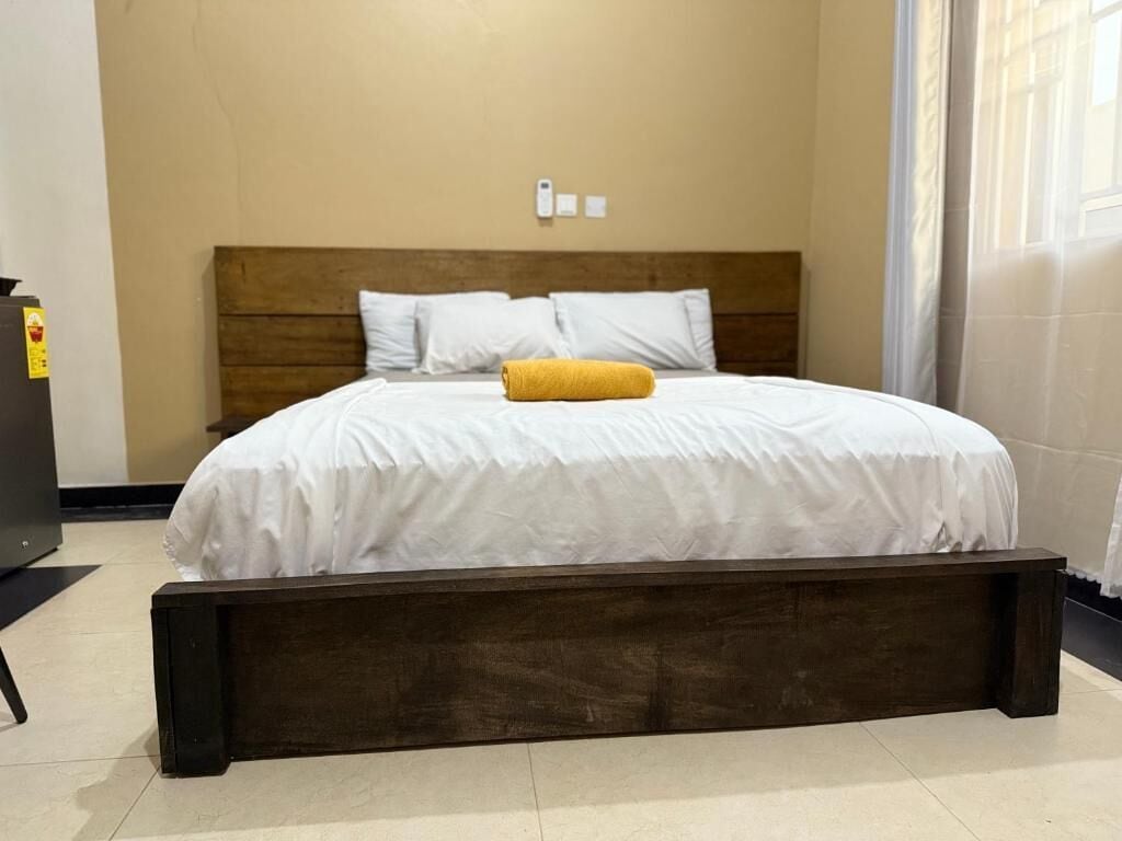 Una cama con cabecera de madera, ropa de cama blanca y almohada amarilla.