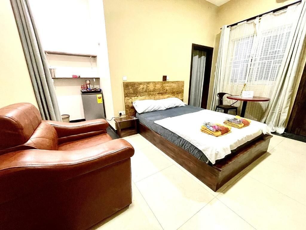 A hotel room with a bed, a brown leather sofa, a small table, and a window with curtains.
