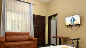 Quarto de hotel com cama, sofá de couro marrom, televisão na parede e uma pequena mesa.