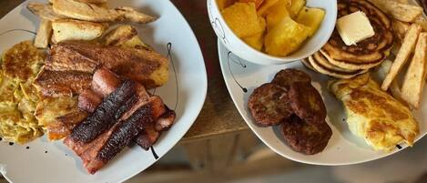 A breakfast plate with eggs, bacon, toast, pancakes, and fruit.