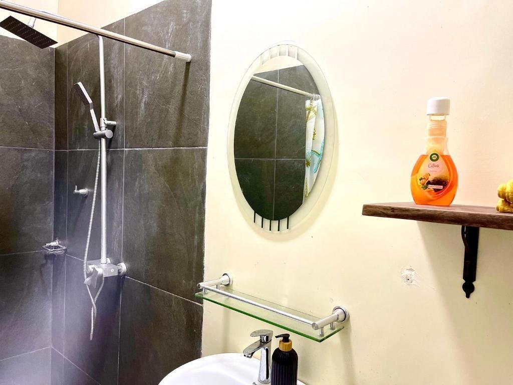 A bathroom with a shower, a round mirror, a glass shelf, and a soap dispenser.