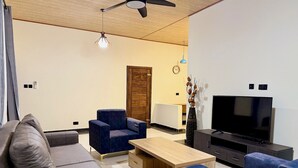 Uma sala de estar moderna com sofá, poltronas, mesa de centro, televisão e ventilador de teto.