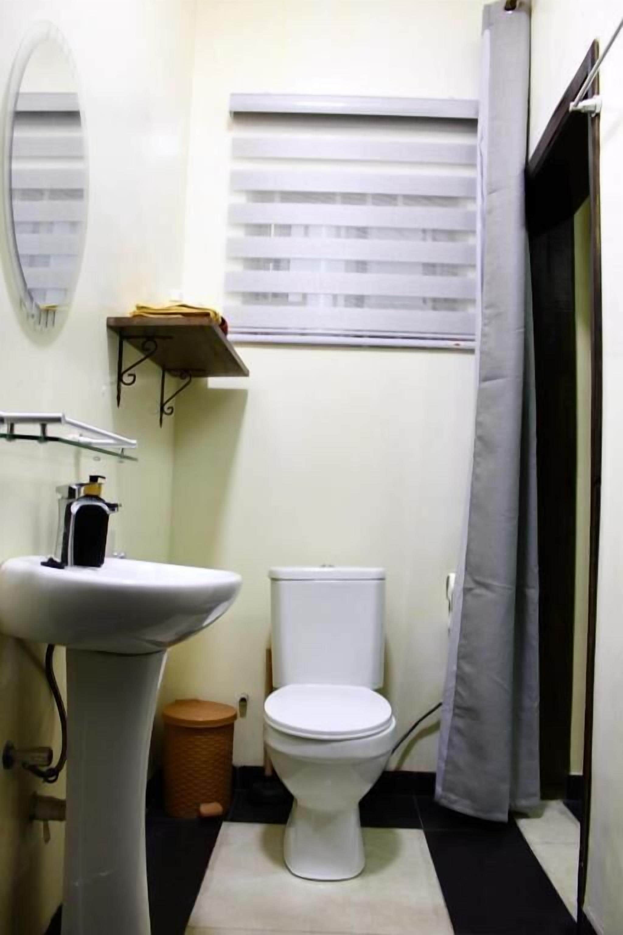 A small bathroom with a pedestal sink, toilet, and a window with blinds.
