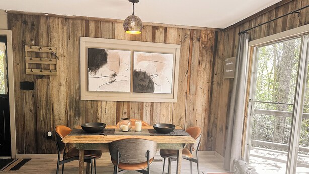 Un coin repas avec une table en bois, quatre chaises et un grand tableau abstrait accroché au mur.