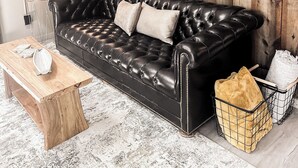 Un canapé en cuir noir avec des coussins, une table basse en bois, une lampe et un tableau accroché à un mur en bois.