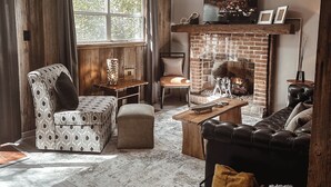 Un salon chaleureux avec une cheminée, des poutres apparentes, un canapé confortable et un coin repas.