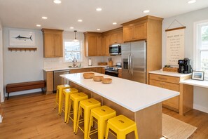 Una cocina moderna con armarios de madera, un refrigerador de acero inoxidable, una isla central con taburetes y vistas al exterior.