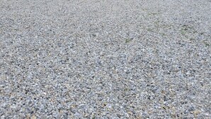 Kaksikerroksinen talo, jossa on etukuisti, pieni puutarha ja sorapäällysteinen ajotie.