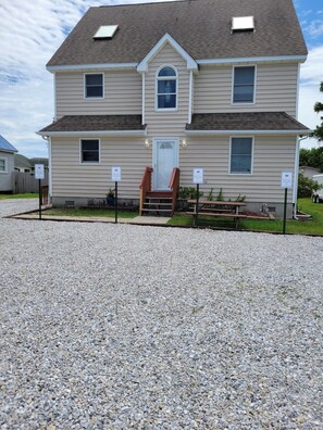 A two-story house with a front porch, a small garden, and a gravel driveway. - Walk to Harborside & Marina|Sleeps 16|Boat Trailer Parking|Minutes to OC Beach (Ocean City)
