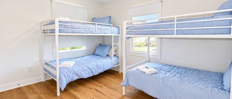 Une chambre avec deux lits superposés, un plancher en bois, un ventilateur de plafond et des fenêtres.