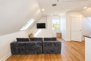 A modern living room with a sloped ceiling, a flat-screen TV mounted on the wall, and a seating area with cushioned benches.