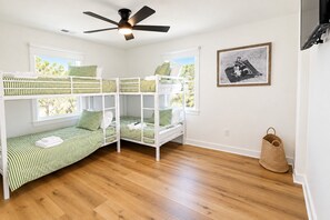 Una habitación con literas, ventilador de techo, cuadro enmarco y cesta tejida.