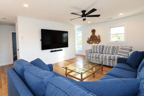 A living room with a large flat-screen TV, a ceiling fan, a striped sofa, and a glass coffee table.