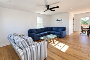 A spacious living room with a large sectional sofa, a glass coffee table, and hardwood flooring.