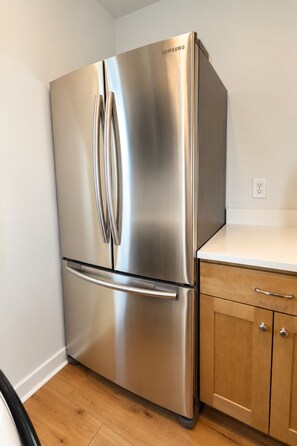 A stainless steel Samsung refrigerator in a kitchen with wooden cabinets and a white countertop.