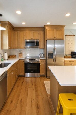A modern kitchen with wooden cabinets, stainless steel appliances, and a yellow stool.