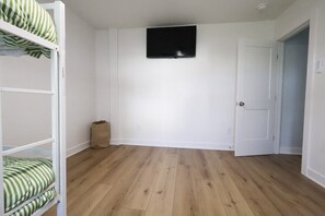A room with a bunk bed, a television mounted on the wall, and a door. - Walk to Harborside & Marina|Sleeps 16|Boat Trailer Parking|Minutes to OC Beach (Ocean City)