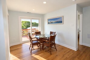 A dining area with a glass table and wicker chairs, a painting on the wall, and a view through a sliding glass door.