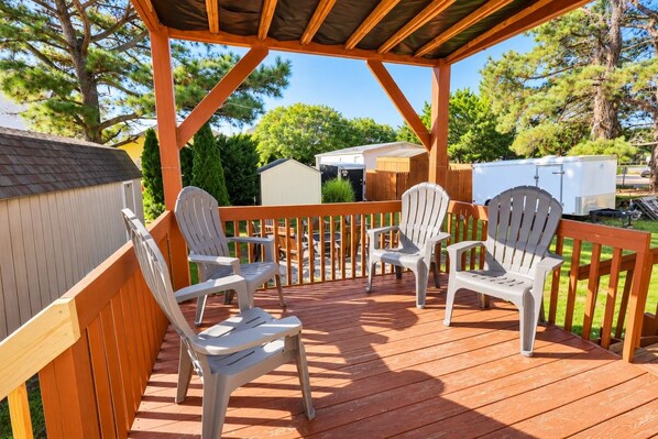 A covered deck with wooden railings and plastic Adirondack chairs.
