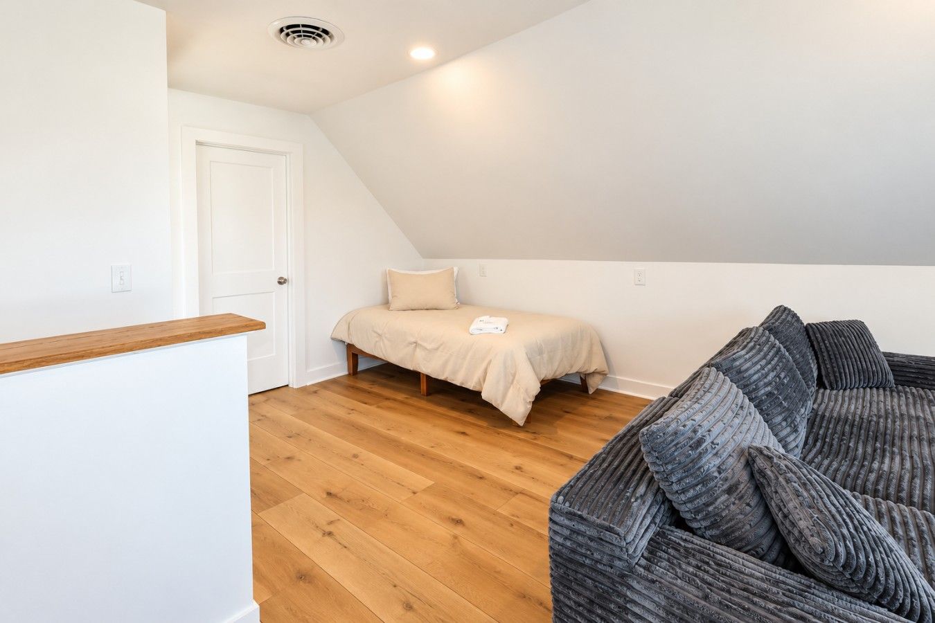 Ein Schlafzimmer mit einem Bett, Holzboden, einer weißen Tür und einem grauen Sofa.