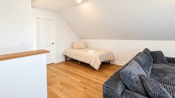 Ein Schlafzimmer mit einem Bett, Holzboden, einer weißen Tür und einem grauen Sofa.