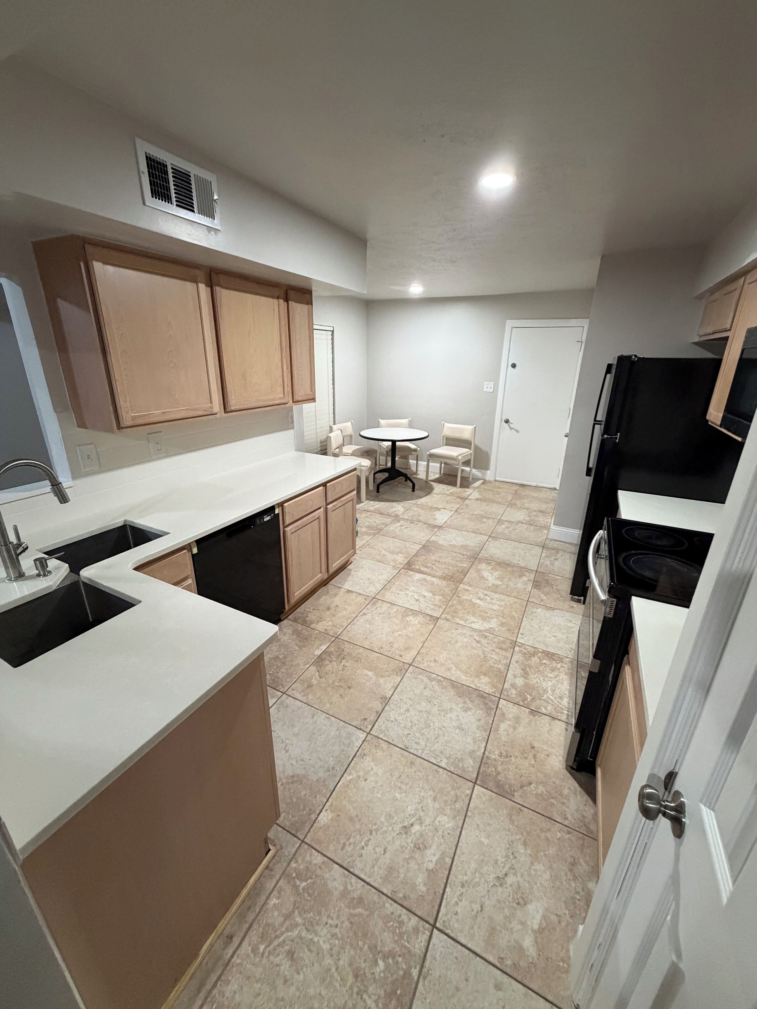 A kitchen with a sink, stove, and cabinets. There is a dining table with chairs in the background.
