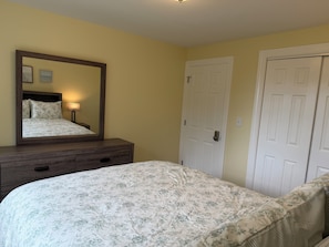 Un dormitorio con cama, cómoda, espejo y dos puertas.