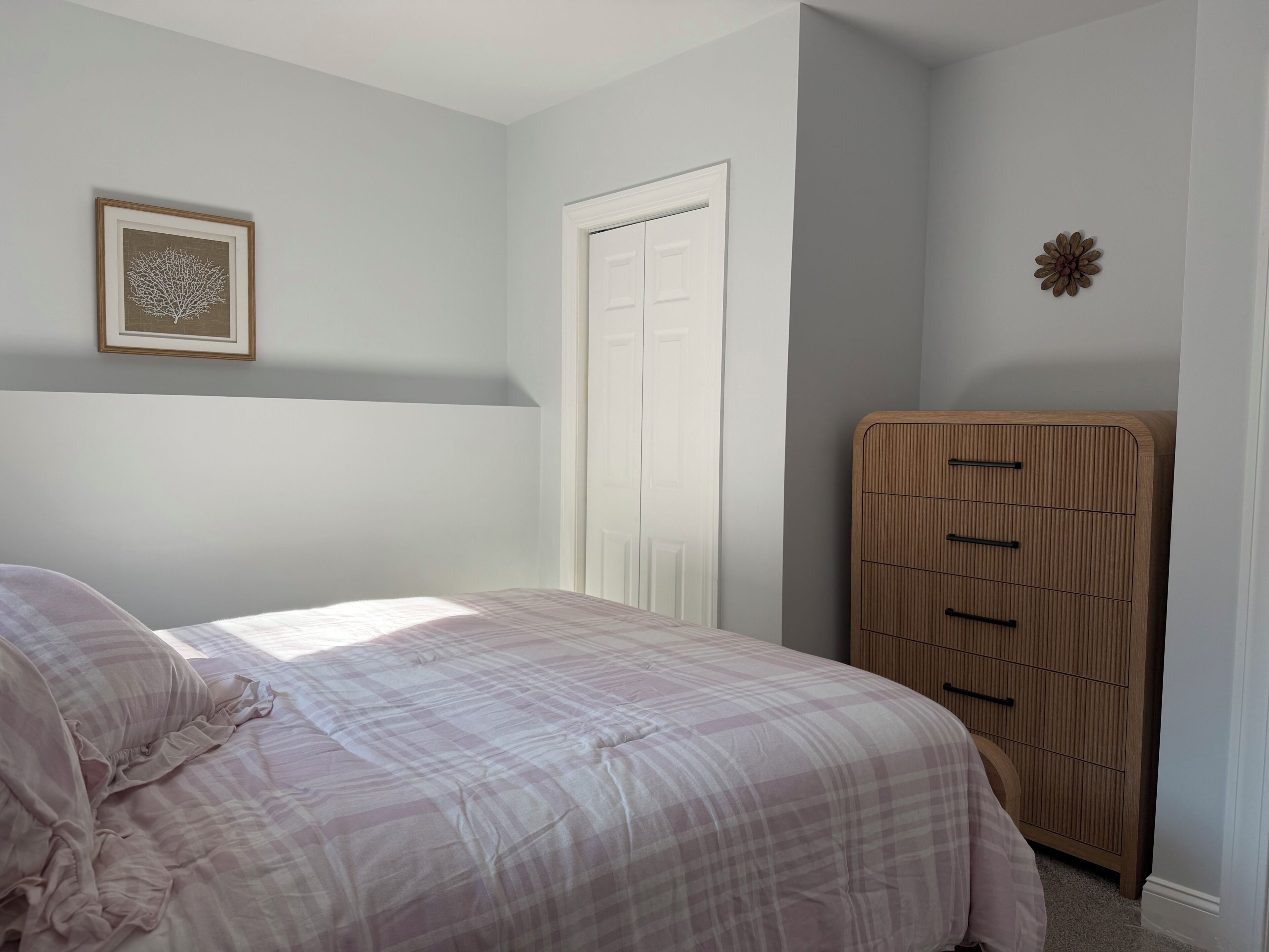 A bedroom with a bed, a dresser, a door, and a wall-mounted picture.