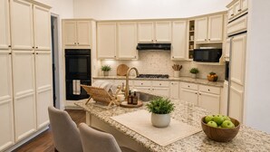 Una cocina con armarios blancos, encimera de granito, estufa integrada y microondas.