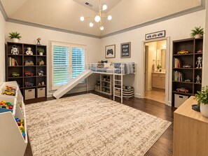 A child's playroom with a bunk bed, shelving with toys, and a slide.