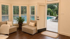 Una habitación con piso de madera, un banco acolchado, una silla y una puerta que da a una zona de piscina.