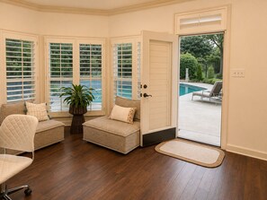 A room with a wooden floor, a cushioned bench, a chair, and a door leading to a pool area.