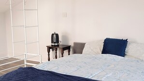 Un dormitorio con cama, mesita de noche, tetera y tendedero.