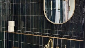 Un baño con lavamanos blanco, grifo dorado y un espejo encima.