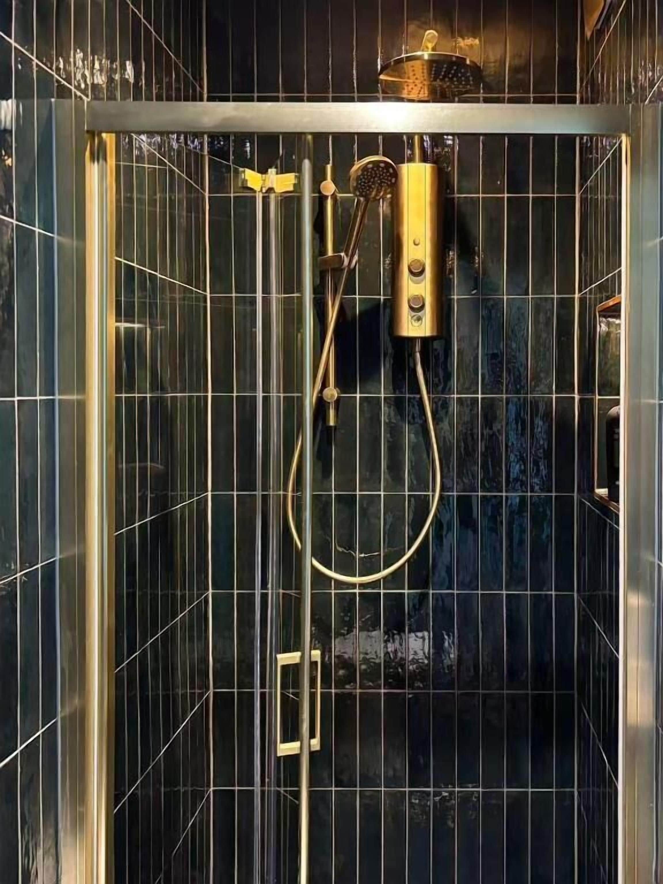 A shower enclosure with a glass door, a handheld showerhead, and a wall-mounted control panel.