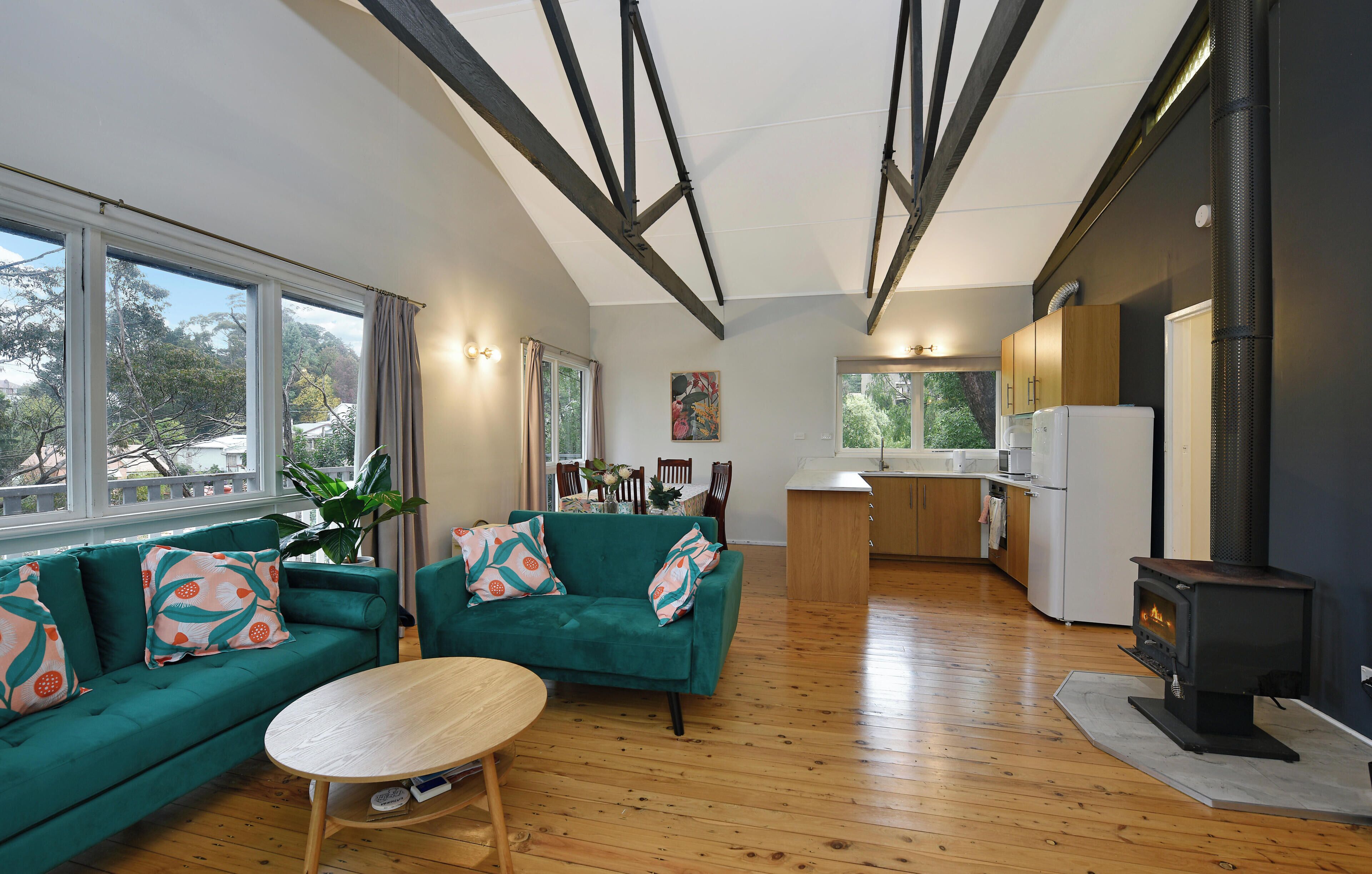A modern living space with a sofa set, a dining table, and a kitchen area with a wood-burning stove.