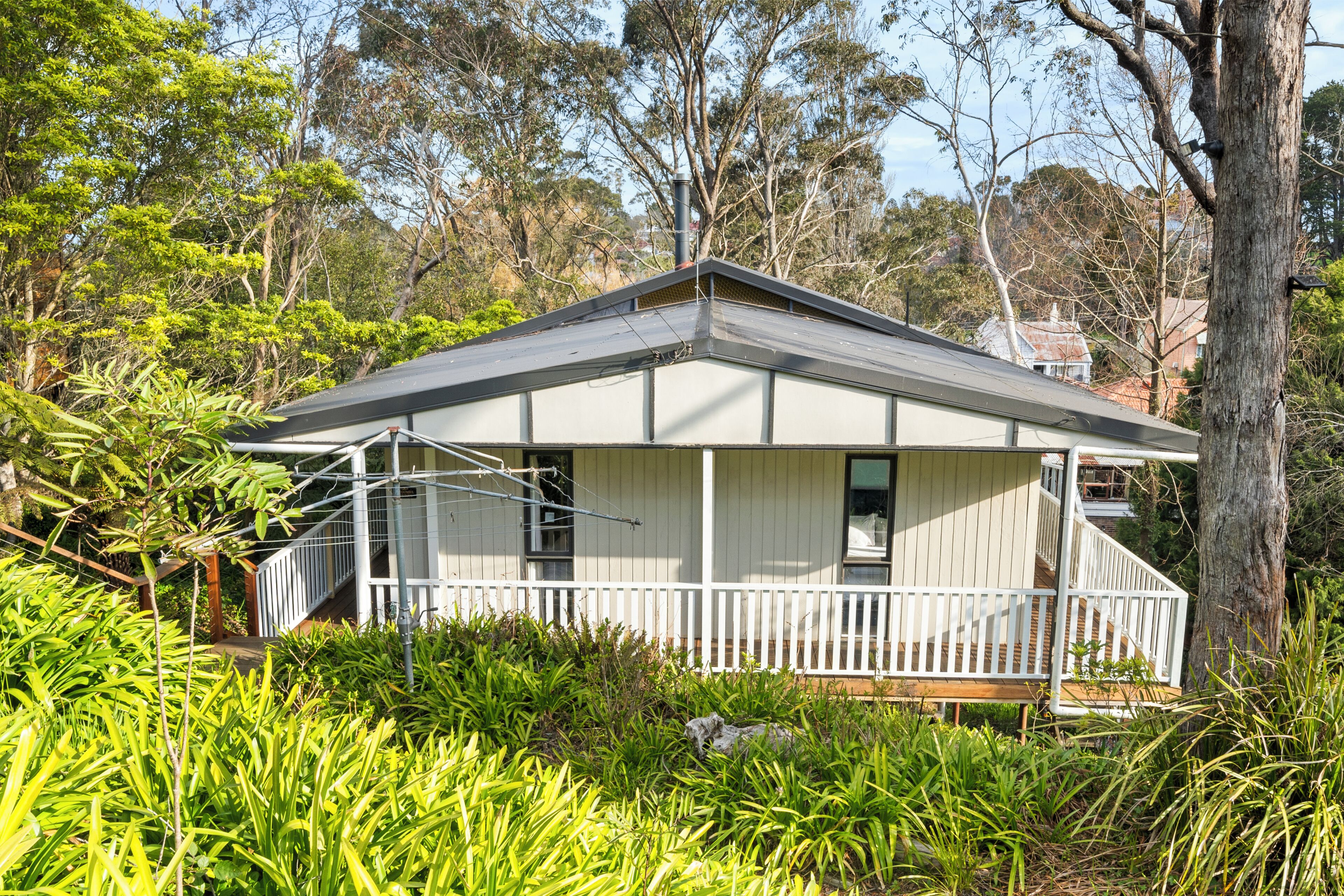 A single-story house with a porch, surrounded by lush greenery and trees.