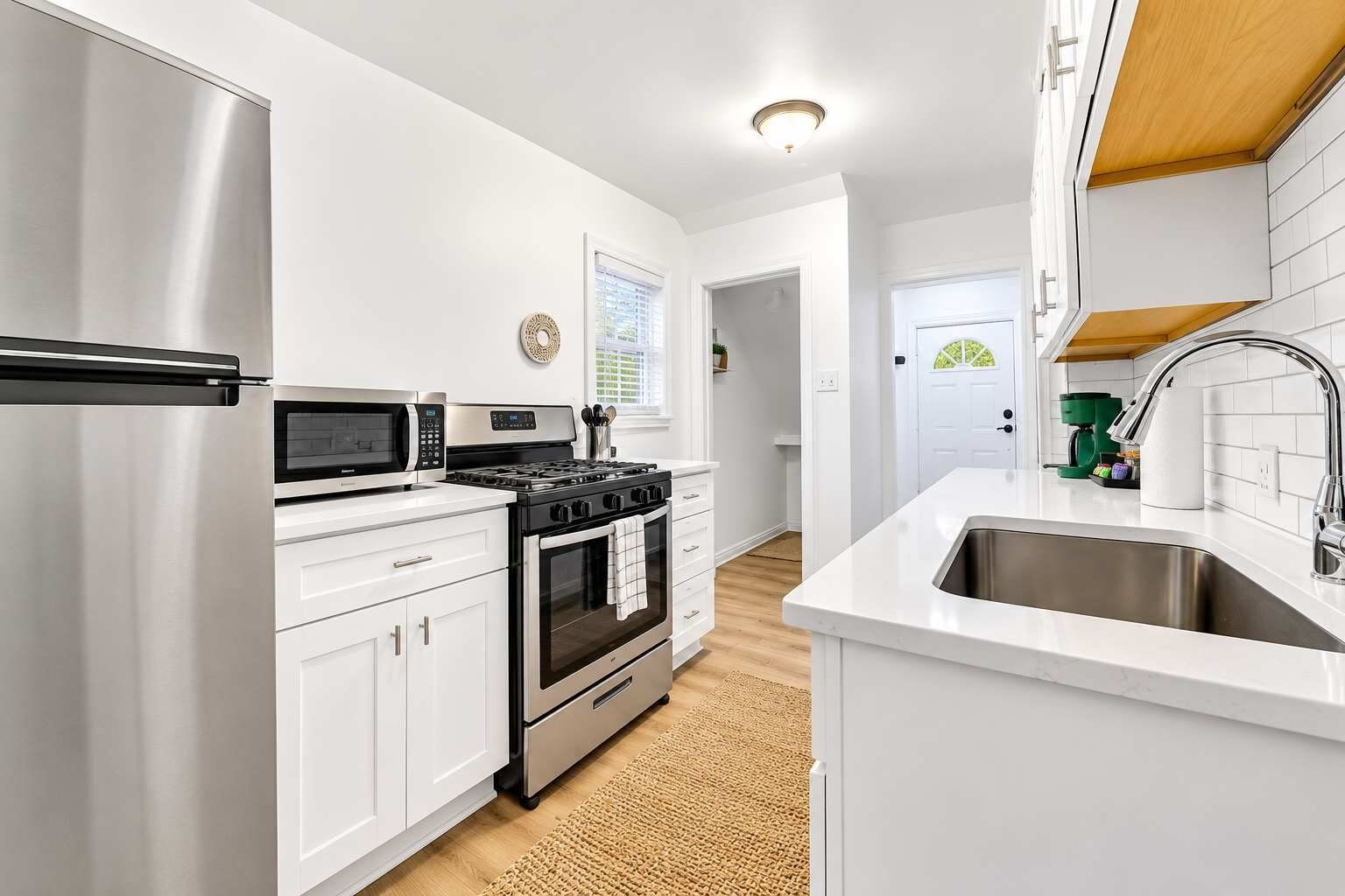 A modern kitchen with stainless steel appliances, white cabinetry, and a wooden floor.