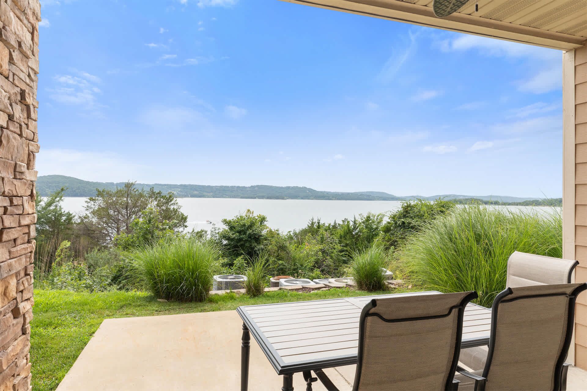 A patio with a table and chairs overlooking a lake with a distant view of hills.