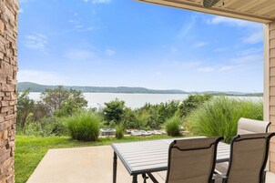 Un patio con mesa y sillas con vista a un lago y colinas a lo lejos.