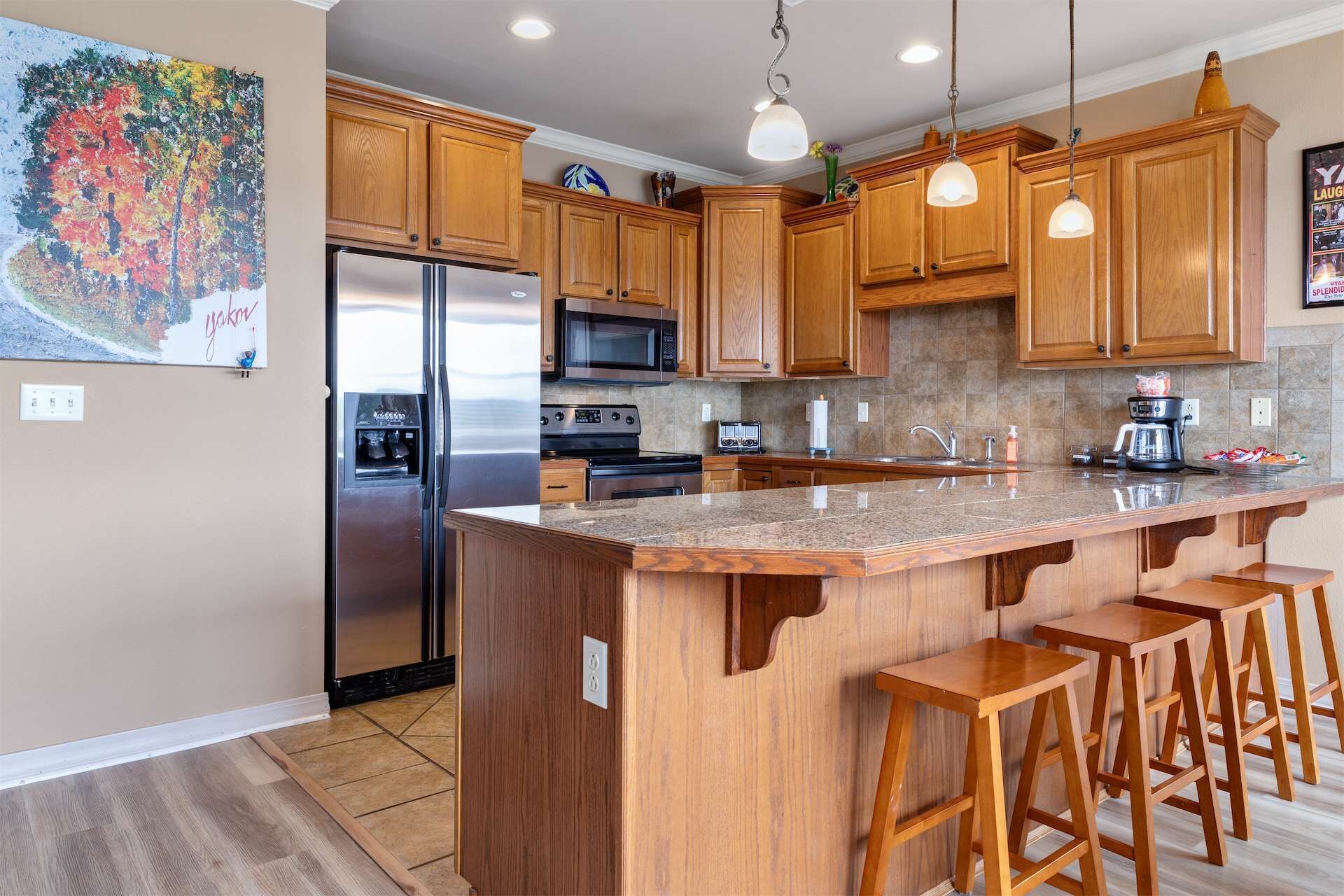 A modern kitchen with wooden cabinets, stainless steel appliances, a granite countertop, and bar stools.