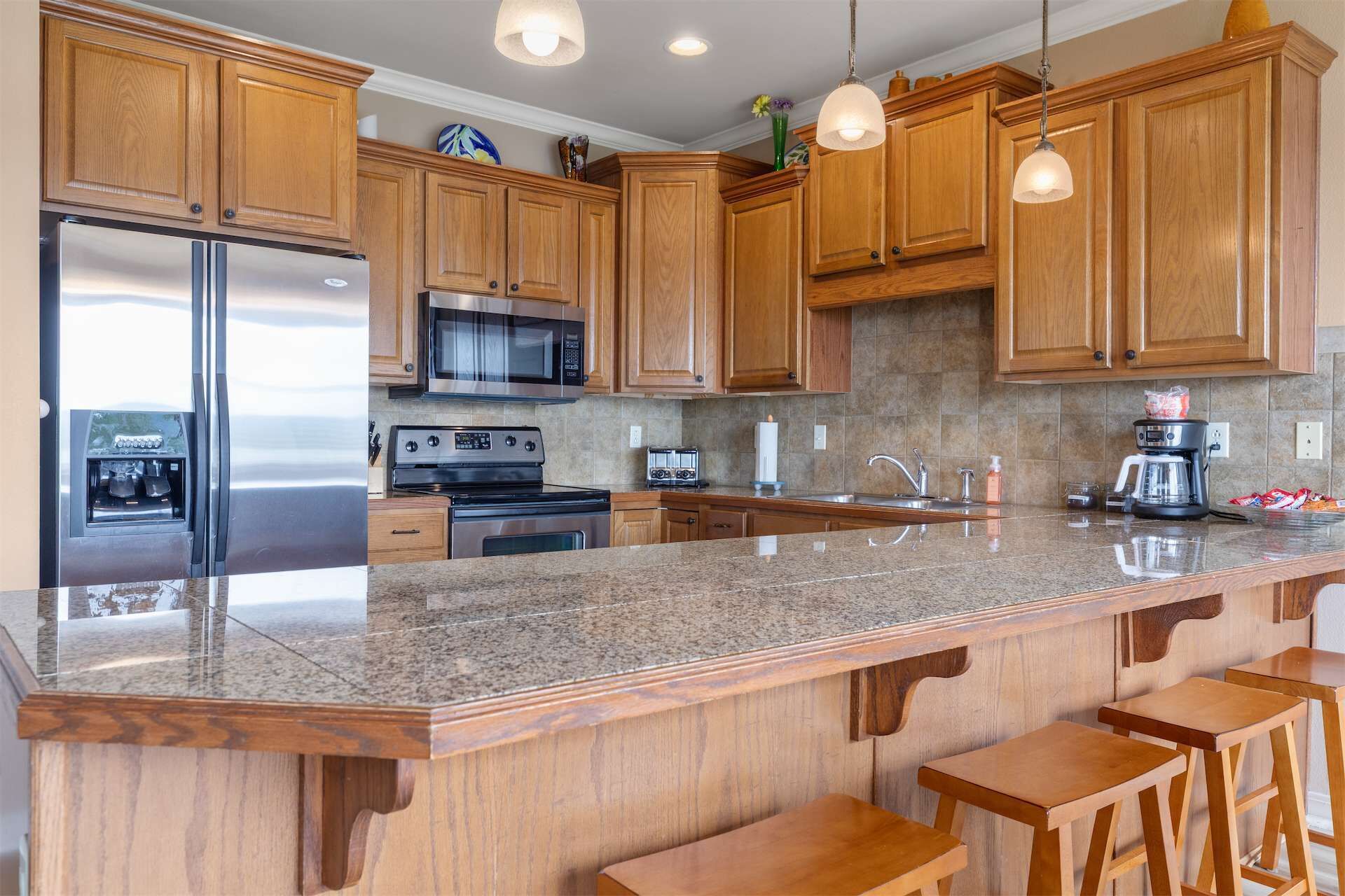 A kitchen with wooden cabinets, stainless steel appliances, granite countertops, and bar stools.