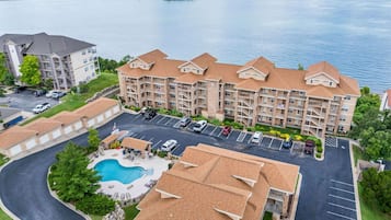 A multi-story hotel with a swimming pool, parking lot, and a view of a lake.