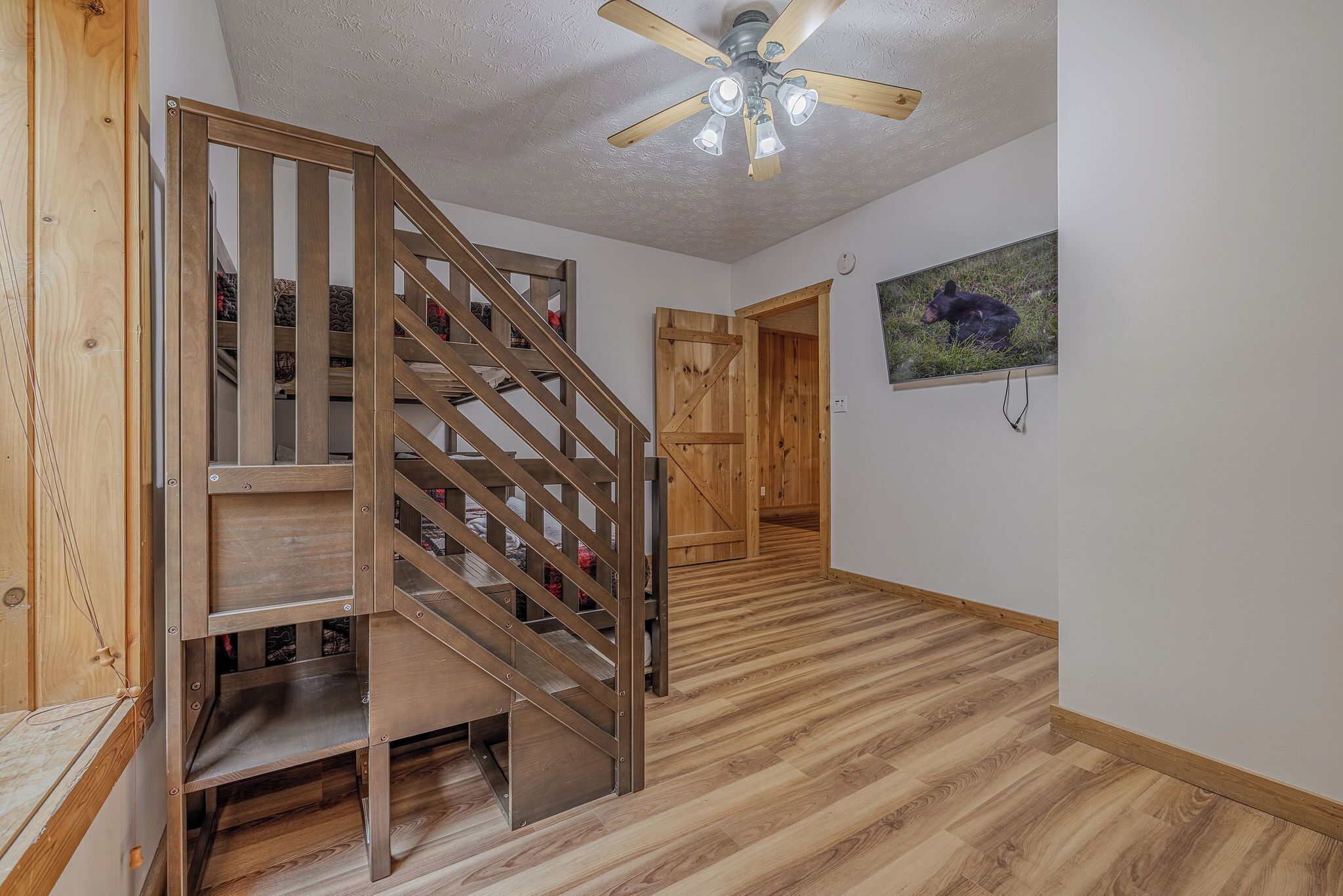 A wooden staircase with a modern ceiling fan, leading to a room with a wooden floor and a bear picture on the wall.