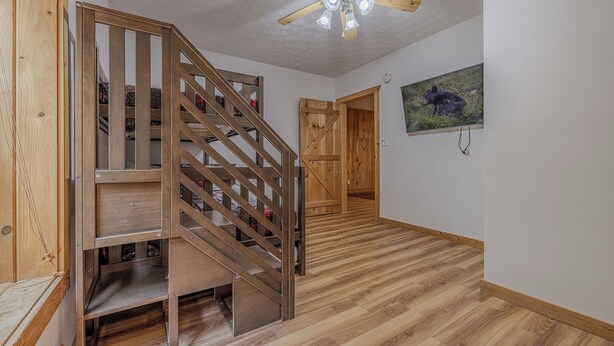 Una escalera de madera con un ventilador de techo moderno, que conduce a una habitación con piso de madera y un cuadro de un oso en la pared.