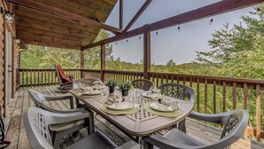 Un espacio de comedor al aire libre con techo, con una mesa lista para cuatro personas, rodeada de sillas y vistas a un paisaje exuberante.