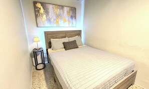 Een slaapkamer met een bed, nachtkastje, lamp en een decoratief kunstwerk aan de muur.
