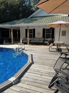 A poolside area with a wooden deck, lounge chairs, a table, and an umbrella.